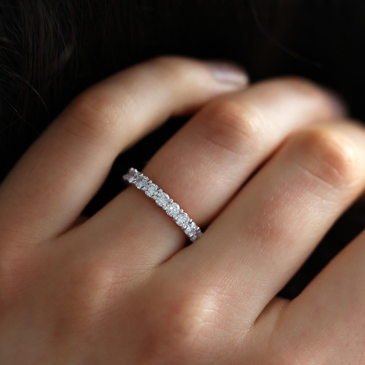 A hand wearing a diamond eternity band in warm, directional light